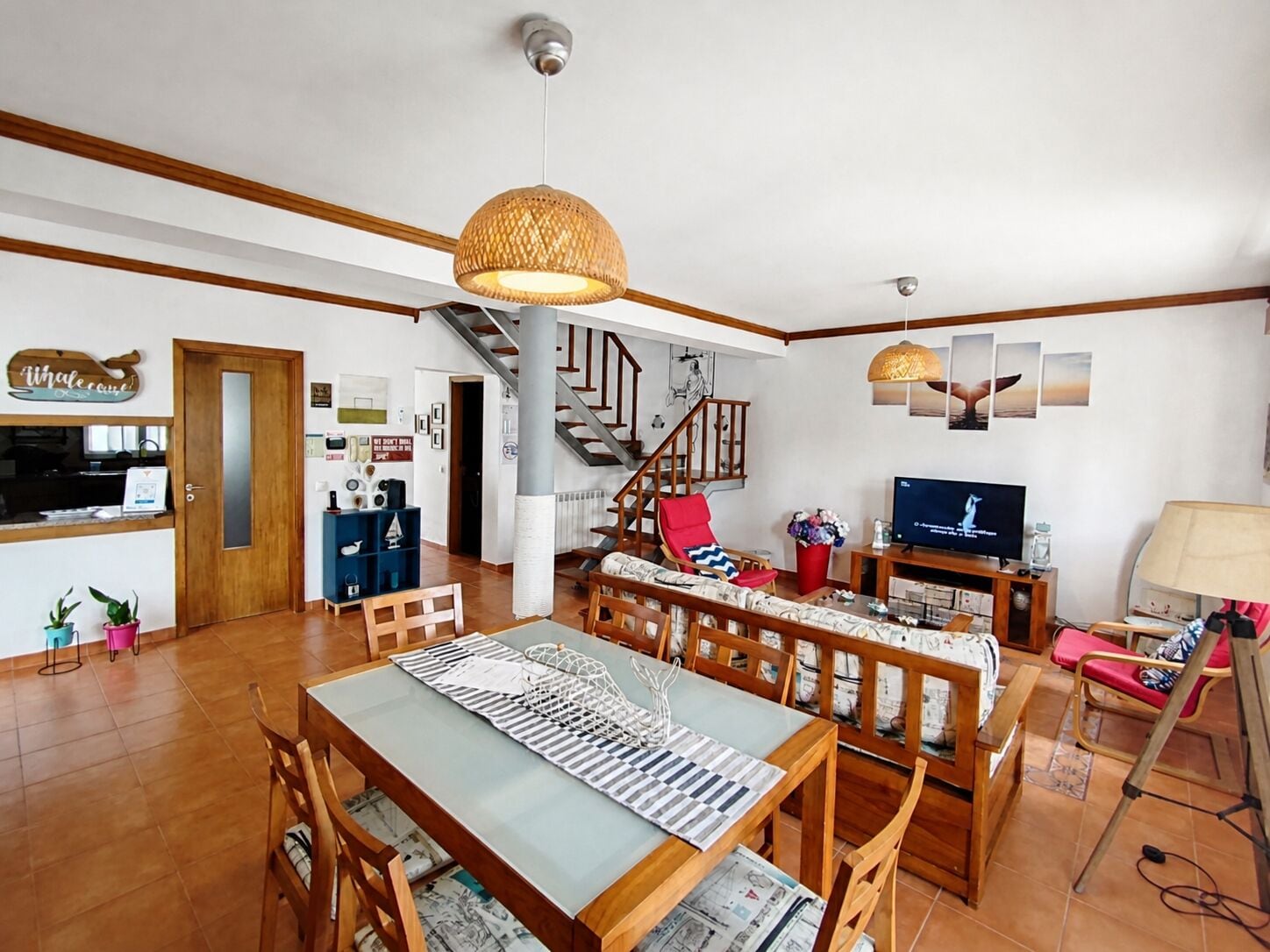 A spacious living area with a dining table, chairs, a sofa, a TV, and a staircase.