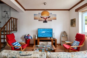 Un salon avec un téléviseur, deux fauteuils rouges, une table basse et une bibliothèque.