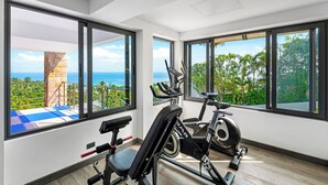 Ein modernes Fitnessstudio mit großen Fenstern, Trainingsgeräten und Blick auf das Meer und viel Grün.