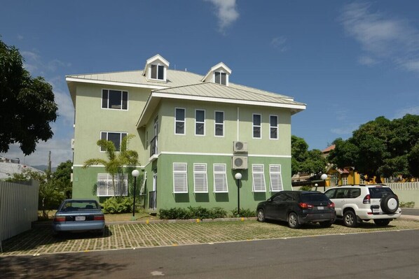 A two-story building with a flat roof, multiple windows, and a parking area with several cars.