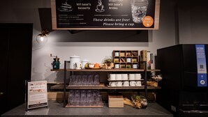 A coffee shop counter with a menu board, free drink sign, and a variety of mugs and glasses. - HOTEL WILL BASE Tsurumi - Adults Only (Yokohama)