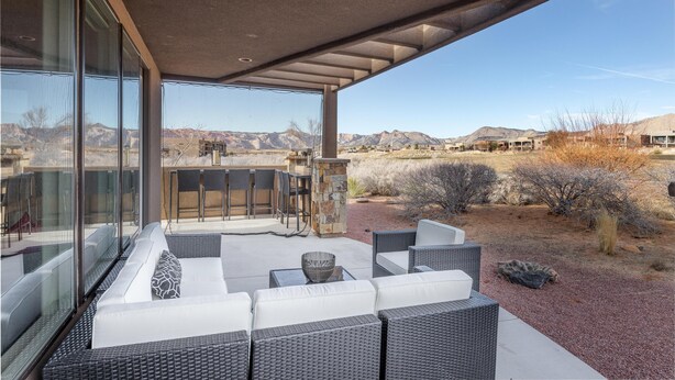 Eine moderne Terrassenausstattung mit Korbmöbeln, einer Steinpfeiler und Blick auf die Wüstenlandschaft.