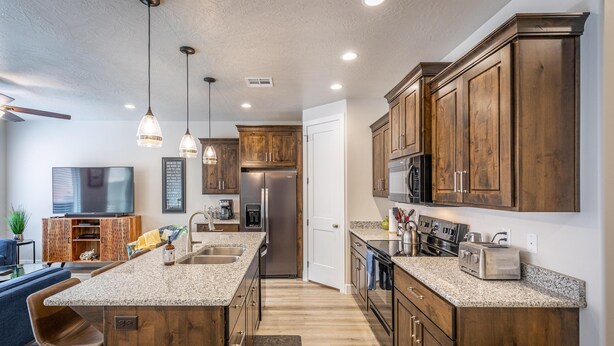 A modern kitchen with wooden cabinets, granite countertops, stainless steel appliances, and pendant lighting. - Overlook Oasis (St. George)