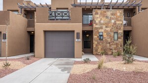 A modern multi-story building with a large garage door, stone facade, and outdoor seating area. - Overlook Oasis (St. George)