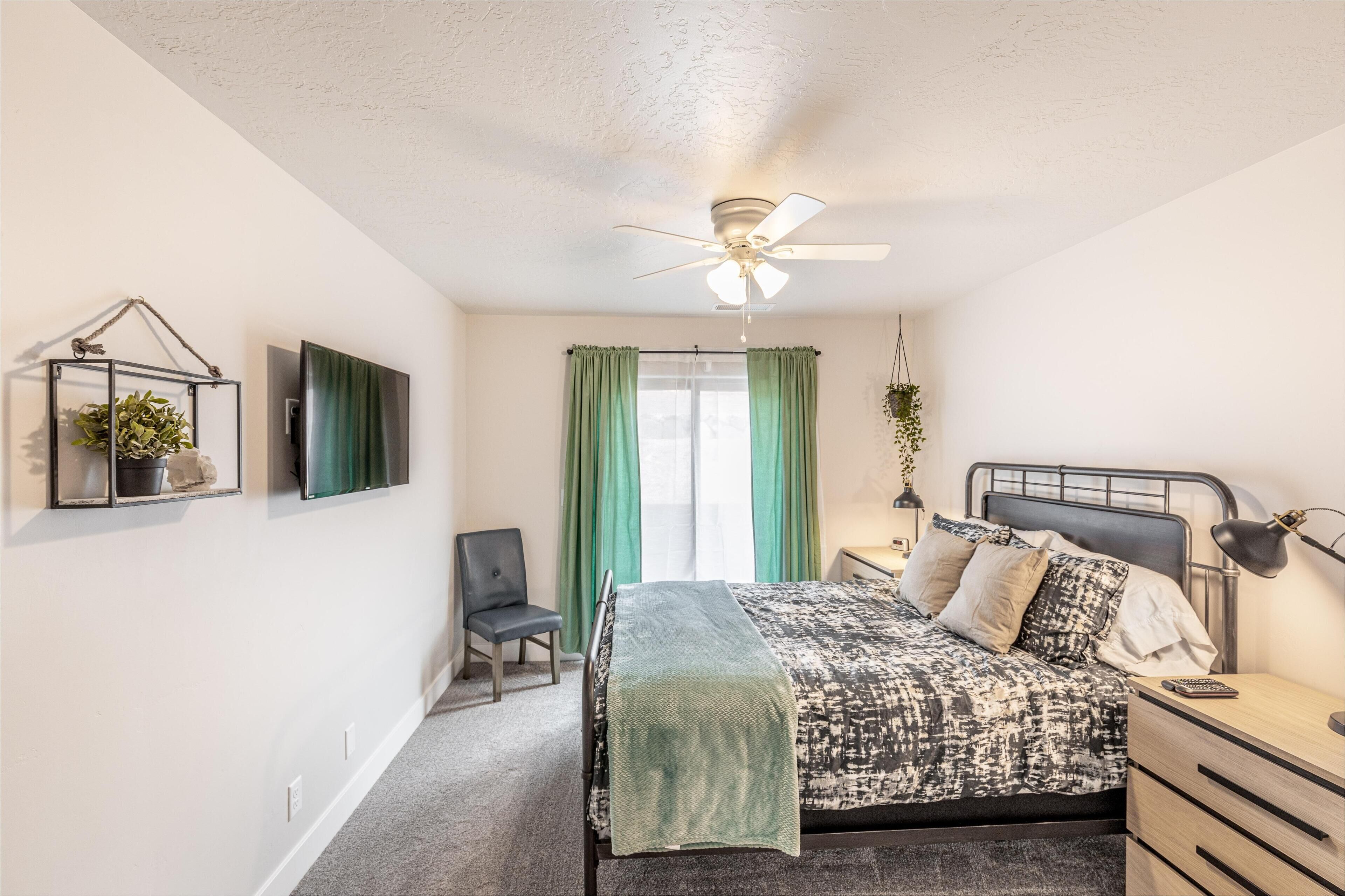 A bedroom with a bed, bedside table, lamp, chair, and a ceiling fan.
