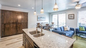 A modern kitchen with granite countertops, wooden cabinets, and pendant lighting. - Overlook Oasis (St. George)