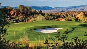 A golf course with a sand bunker, surrounded by rocky terrain and sparse vegetation. - Overlook Oasis (St. George)