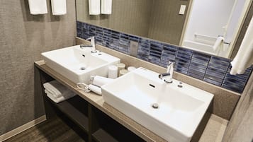 A modern bathroom with two sinks, a mirror, and a towel rack.