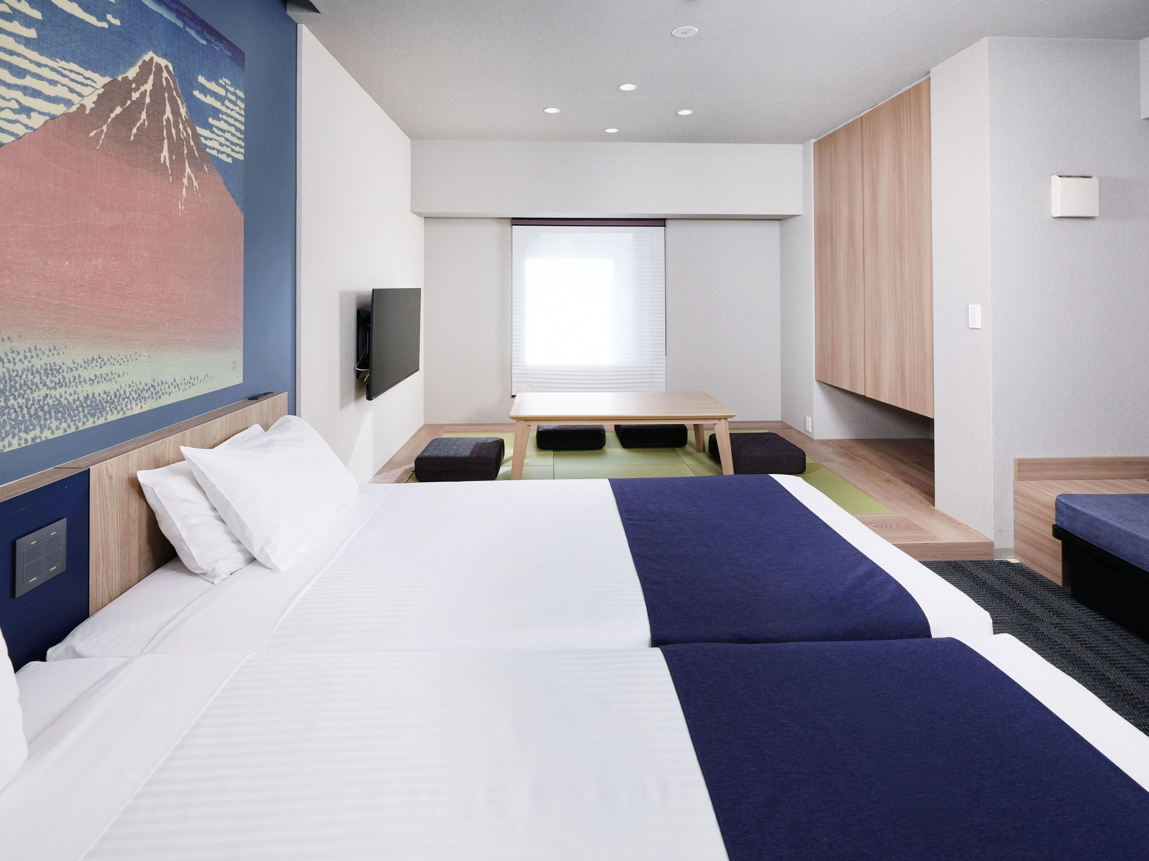 A modern hotel room with a large bed, a small table, a TV, and a painting of a mountain.