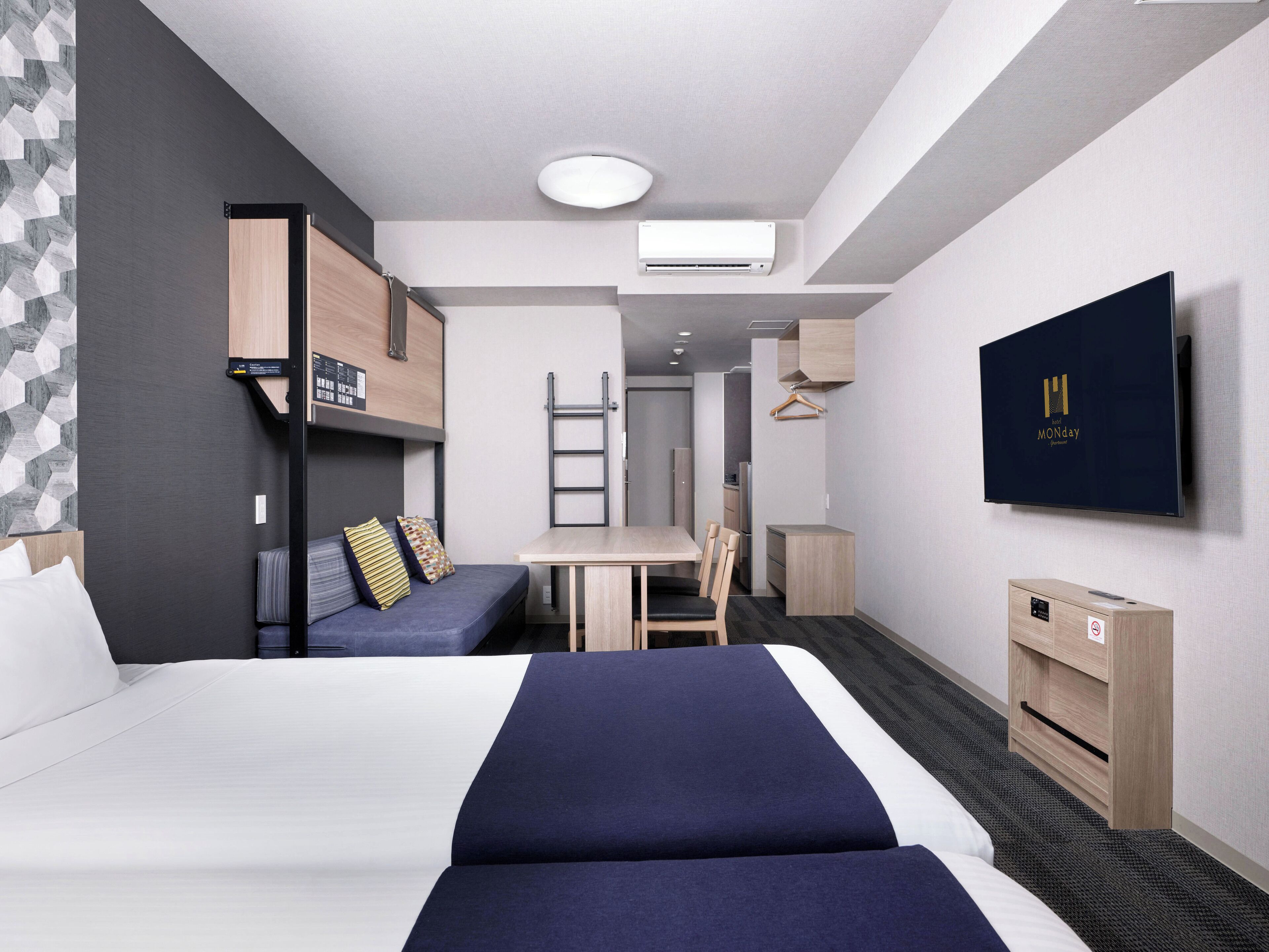 A modern hotel room with a large bed, a desk, a chair, a TV, and a wardrobe.