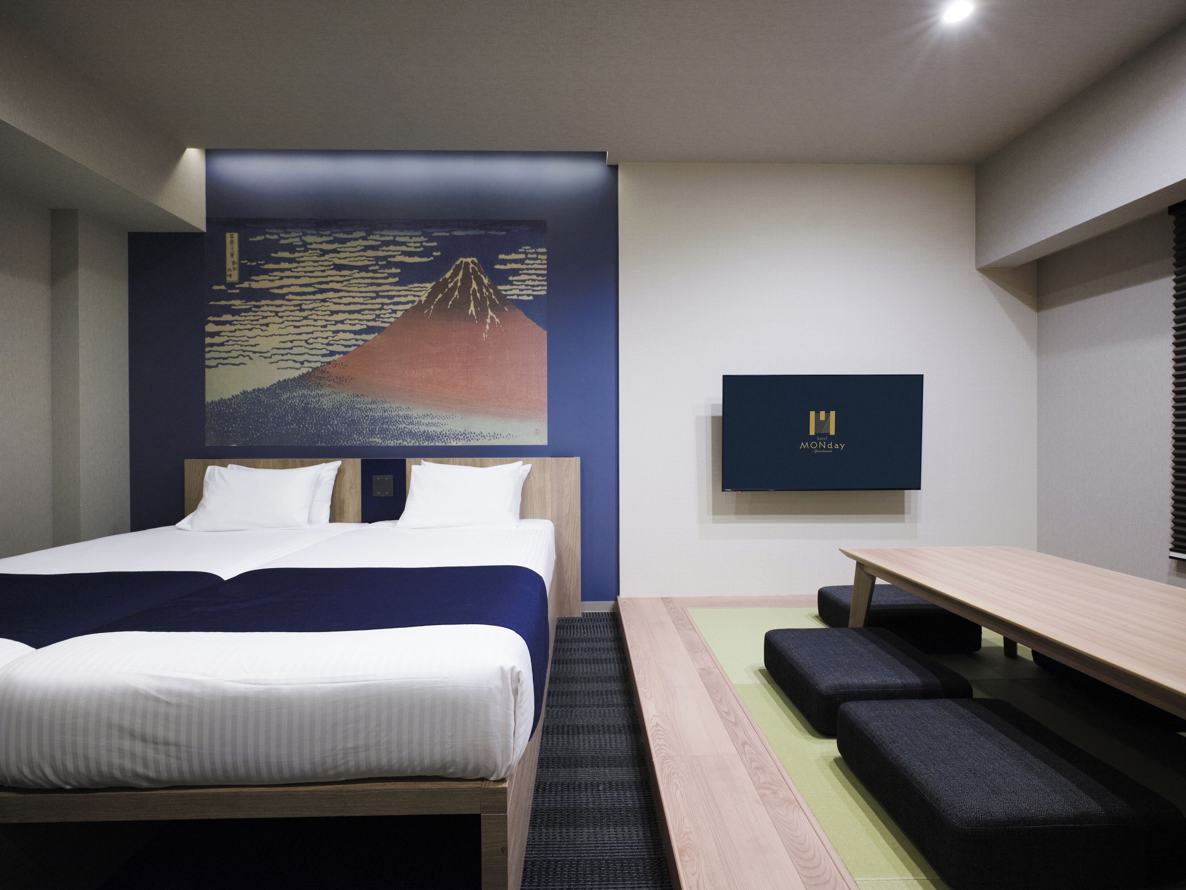 Habitació d'hotel moderna amb un llit, escriptori, una banca, un quadre de muntanya i una televisió penjada a la paret.