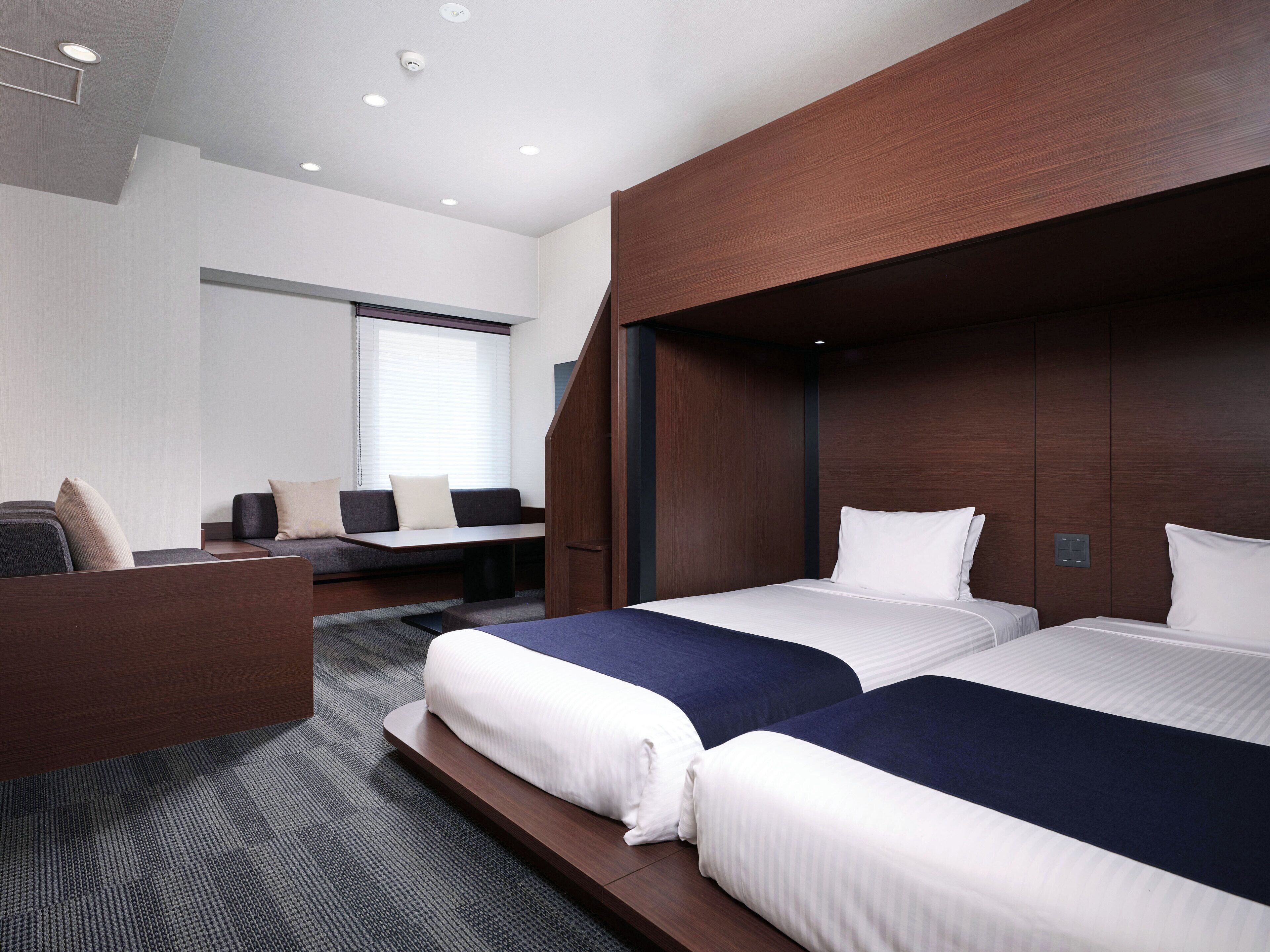 A modern hotel room with two beds, a desk, and a seating area.