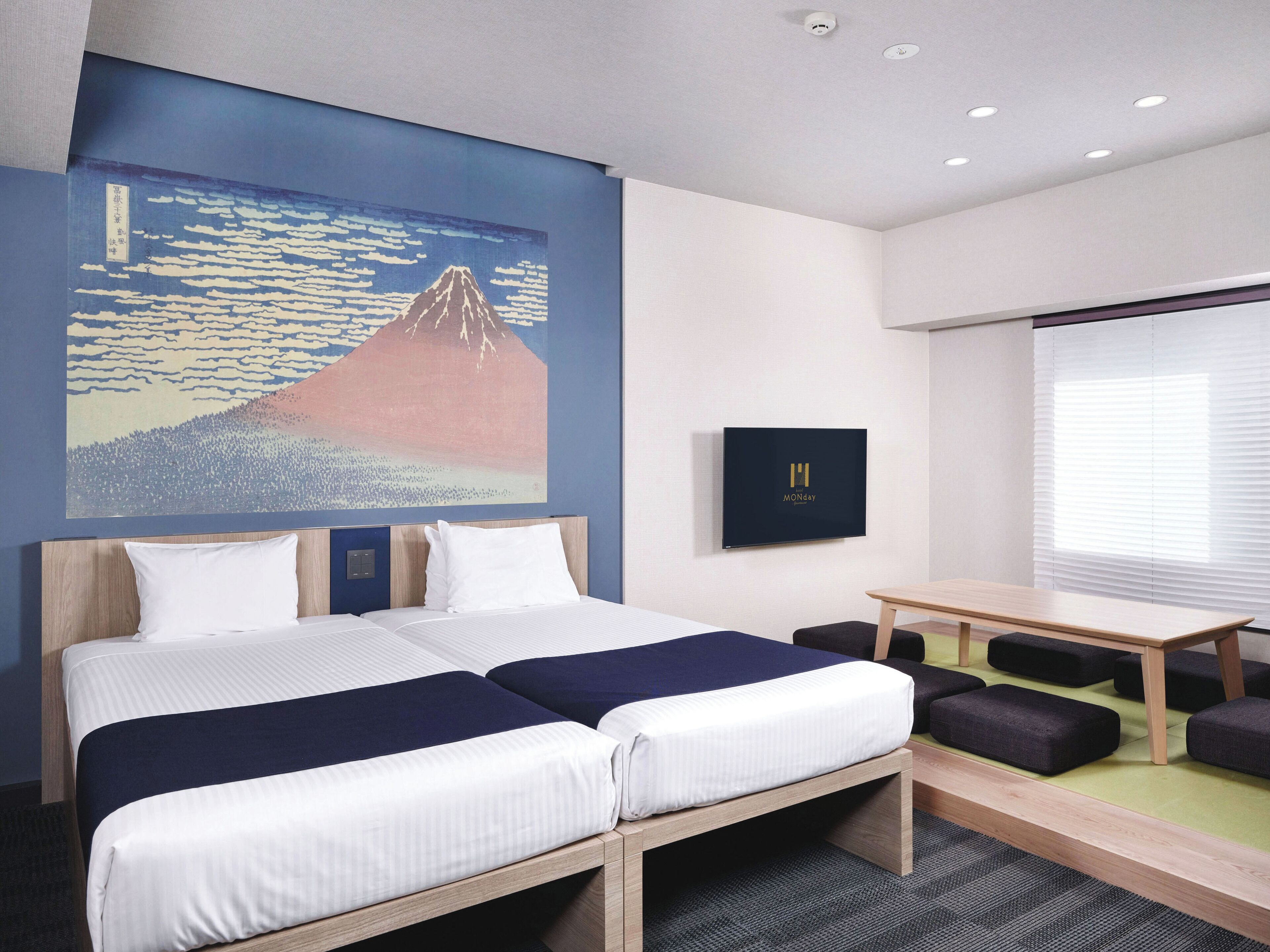 A hotel room with a bed, a desk, and a wall-mounted TV.