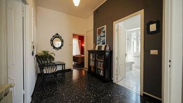 A hallway with a black speckled floor, a potted plant, a black chair, a bookshelf, and a door leading to another room.