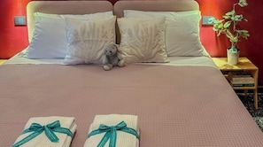 A bed with two pillows, a teddy bear, and two wrapped towels.