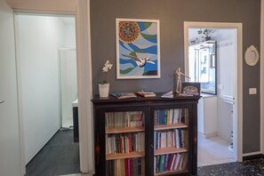 A hallway with a bookshelf, a framed artwork, and a potted plant.