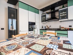 A kitchen with a patterned tablecloth, a bottle, and a cup on the table.