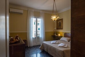 Habitación de hotel con cama, escritorio con un oso de peluche, lámpara colgante y ventana con vistas.