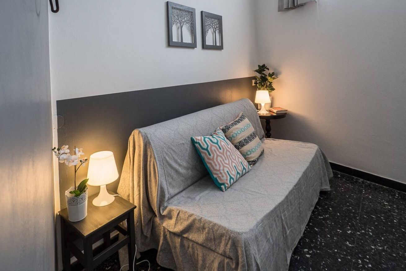 A bedroom with a bed, bedside table with a lamp, a potted plant, and two wall-mounted picture frames.