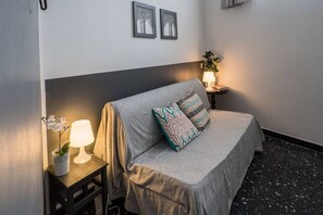 Ein Schlafzimmer mit Bett, Nachttisch mit Lampe, einer Topfpflanze und zwei Bilderrahmen an der Wand.