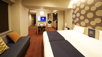 A hotel room with a large bed, a sofa, a dining table with chairs, a washing machine, and a television.