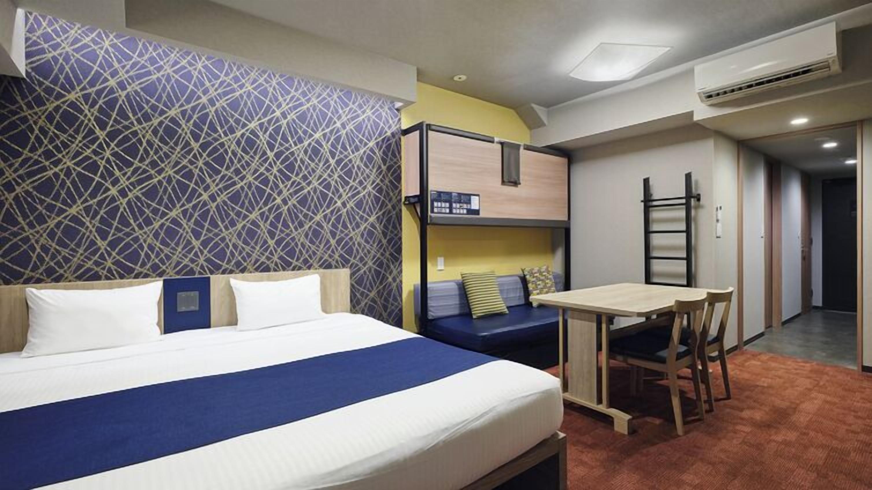 A hotel room with a bed, a desk, a chair, a bunk bed, and a ladder.