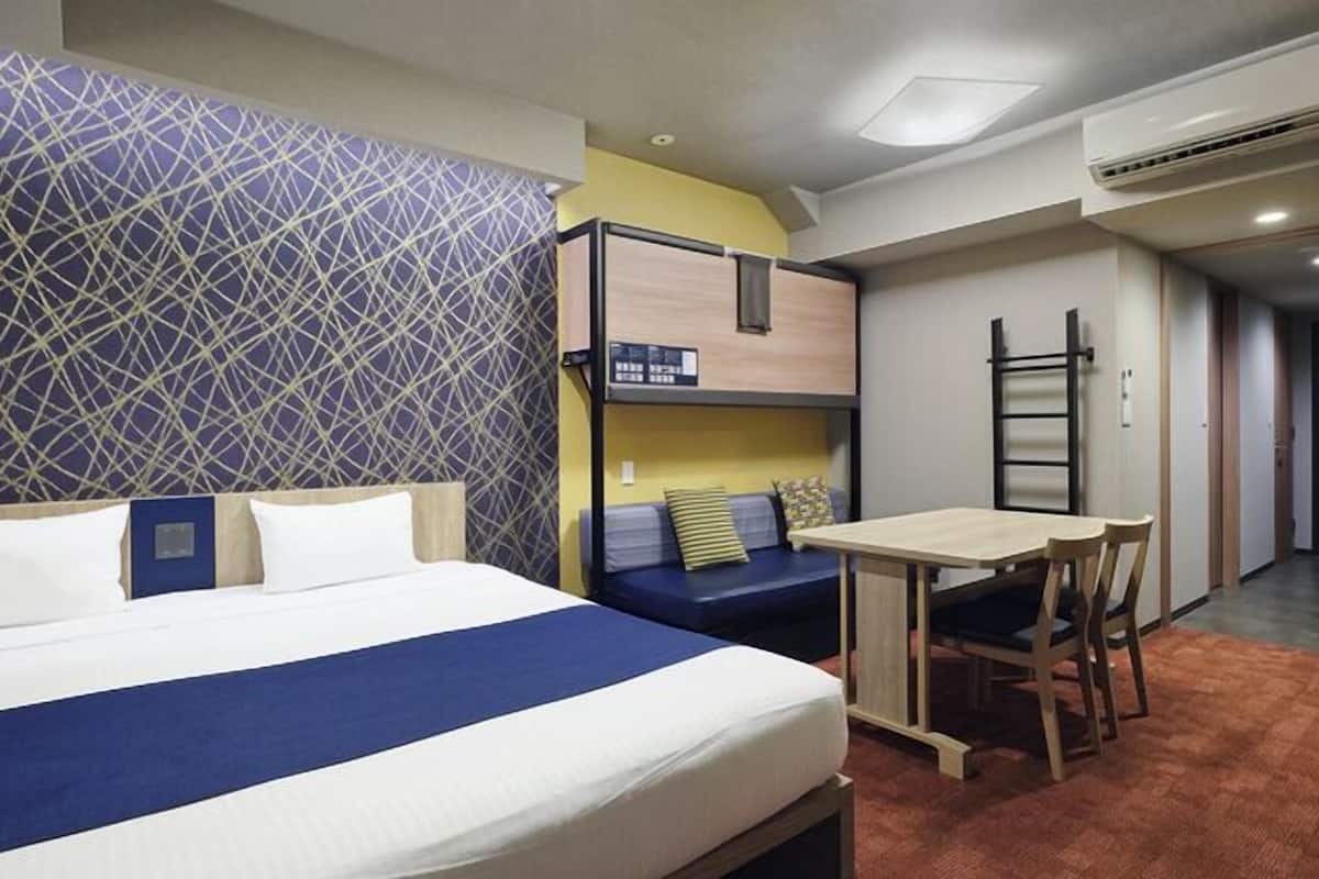 A hotel room with a bed, a desk, a chair, a bunk bed, and a ladder.