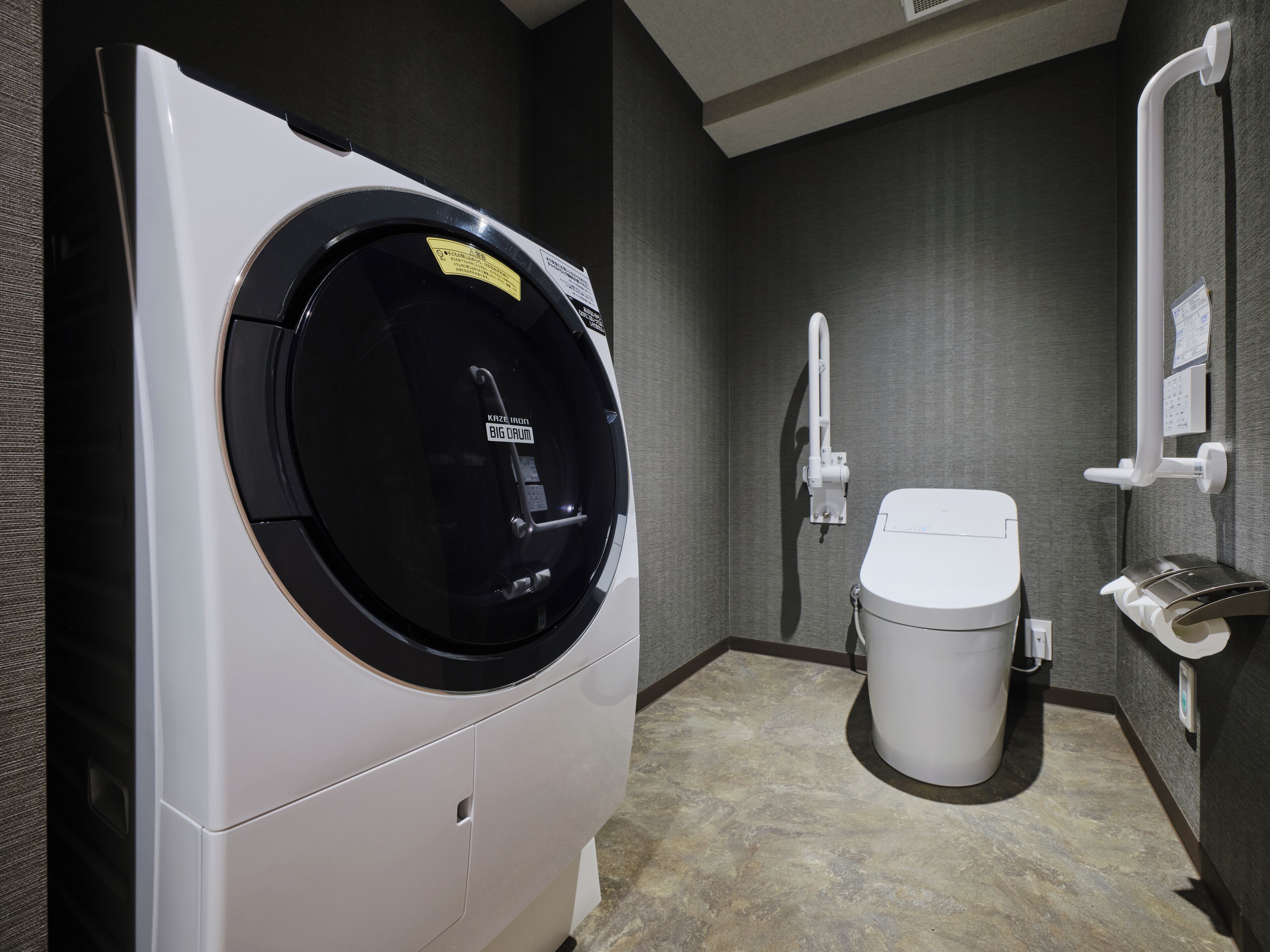 A compact, modern bathroom with a built-in washer and dryer, a toilet, and a handrail for accessibility.