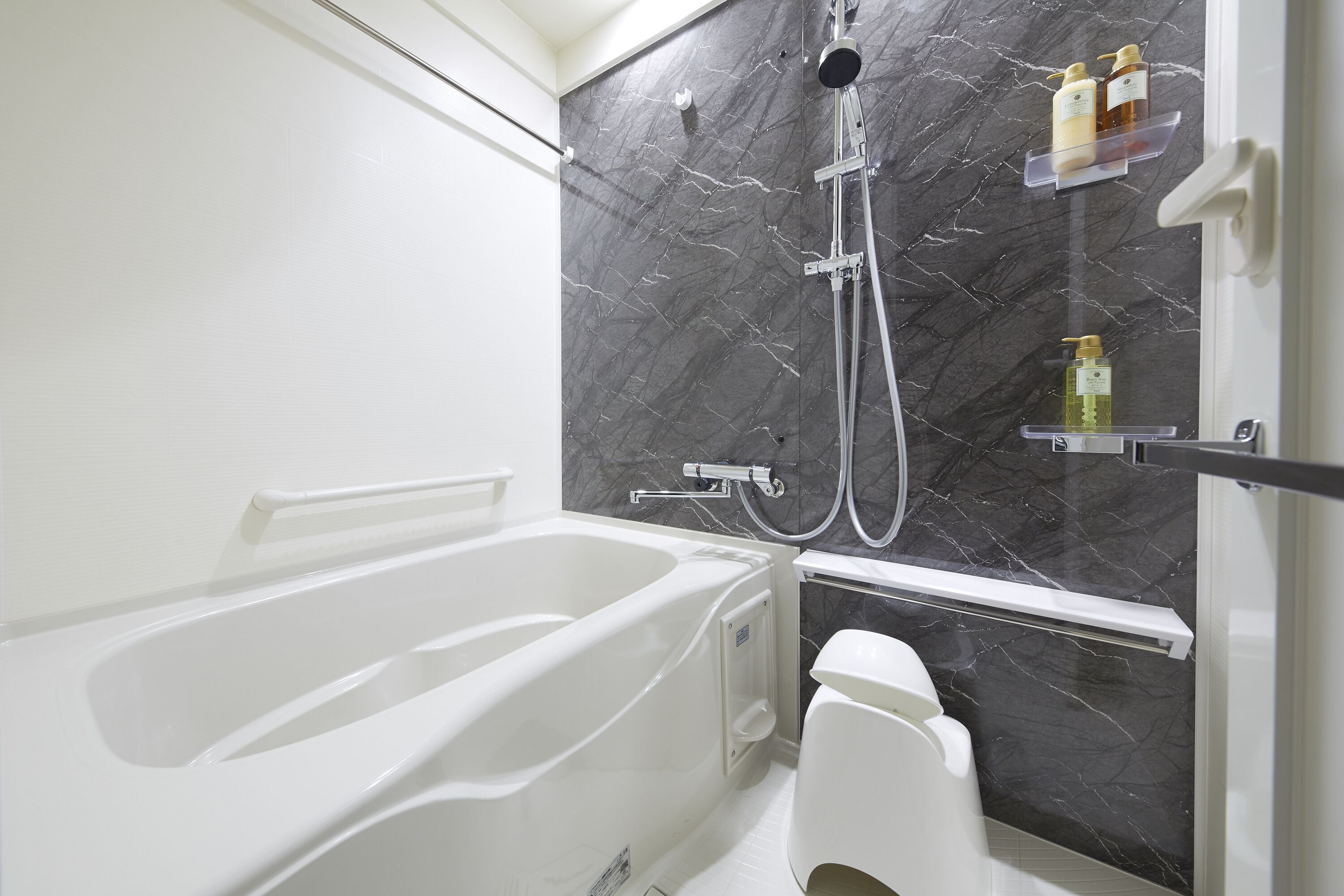 A modern bathroom with a white bathtub, a shower with a handheld showerhead, and a marble backsplash.