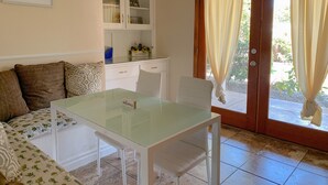 A dining area with a glass table, white chairs, a cushioned bench, a chandelier, a cabinet with glass doors, and a sliding glass door with curtains. - Charming Family House Near Sequoia Park (Visalia)