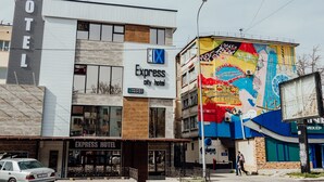 A hotel with a modern design, featuring a sign for 'Express City Hotel' and a colorful mural on the adjacent building. - Express City Hotel (Shymkent)