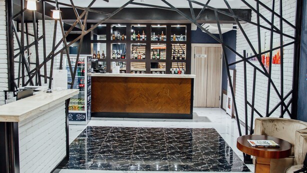 A bar area with a wooden counter and shelves of bottles. - Express City Hotel (Shymkent)