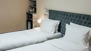 A hotel room with two beds, a bedside table, a lamp, and a wall-mounted air conditioner.