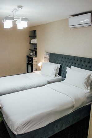 A hotel room with two beds, a bedside table, a lamp, and a wall-mounted air conditioner. - Express City Hotel (Shymkent)