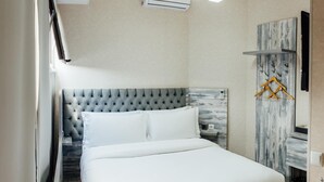 A neatly made bed with a tufted headboard, a wall-mounted air conditioner, and a hanging coat rack. - Express City Hotel (Shymkent)