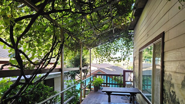 A wooden deck with picnic tables and a railing, overlooking a residential area with houses and a swimming pool. - Ulleung Haeoreum Pension (Ulleung)
