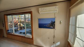 Habitación con un amplio ventanal que da a una obra en construcción, un equipo de aire acondicionado en la pared y un cartel con un paisaje costero.