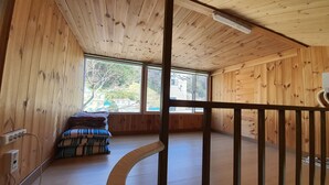 A wooden interior with a curved staircase, large windows, and a bed with striped bedding. - Ulleung Haeoreum Pension (Ulleung)