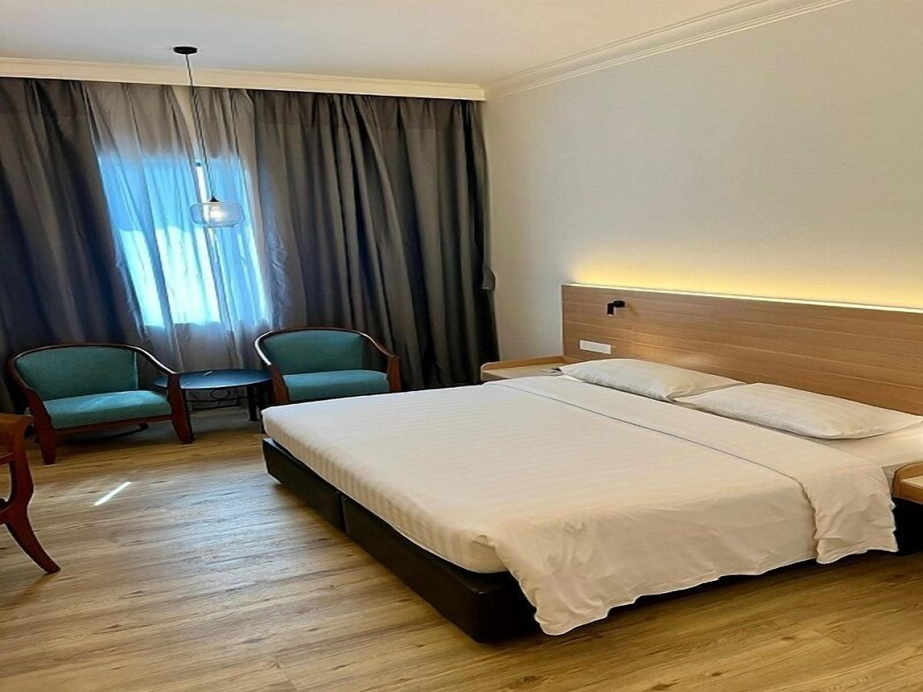 Une chambre d’hôtel avec un grand lit, deux chaises, une petite table et une fenêtre avec des rideaux.