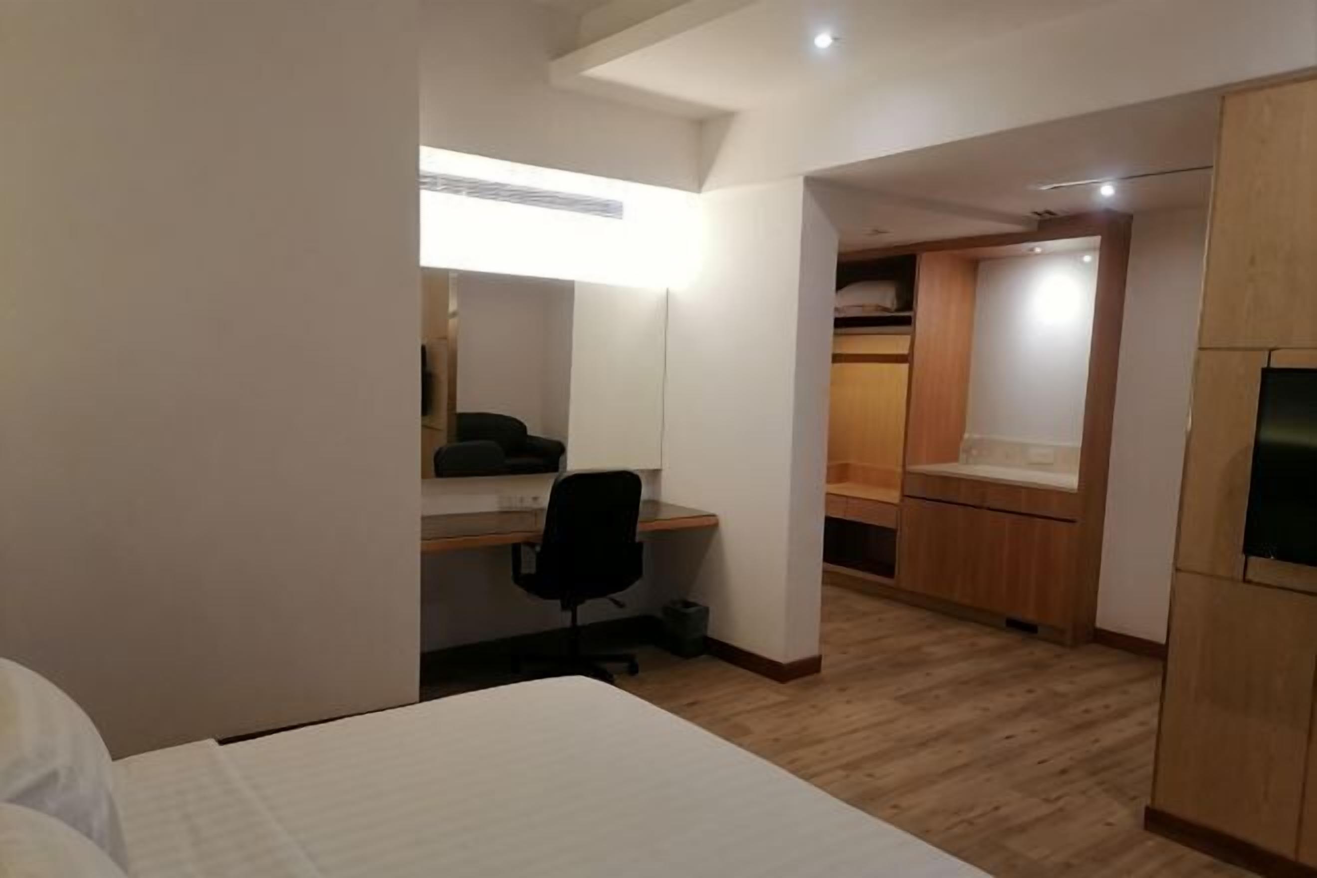 A hotel room with a bed, a desk with a chair, a wardrobe, and a mirror.