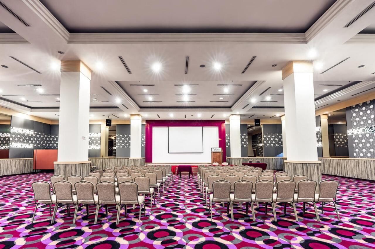 A conference room with rows of chairs, a large screen, and a stage.