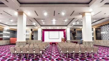 A conference room with rows of chairs, a large screen, and a stage.