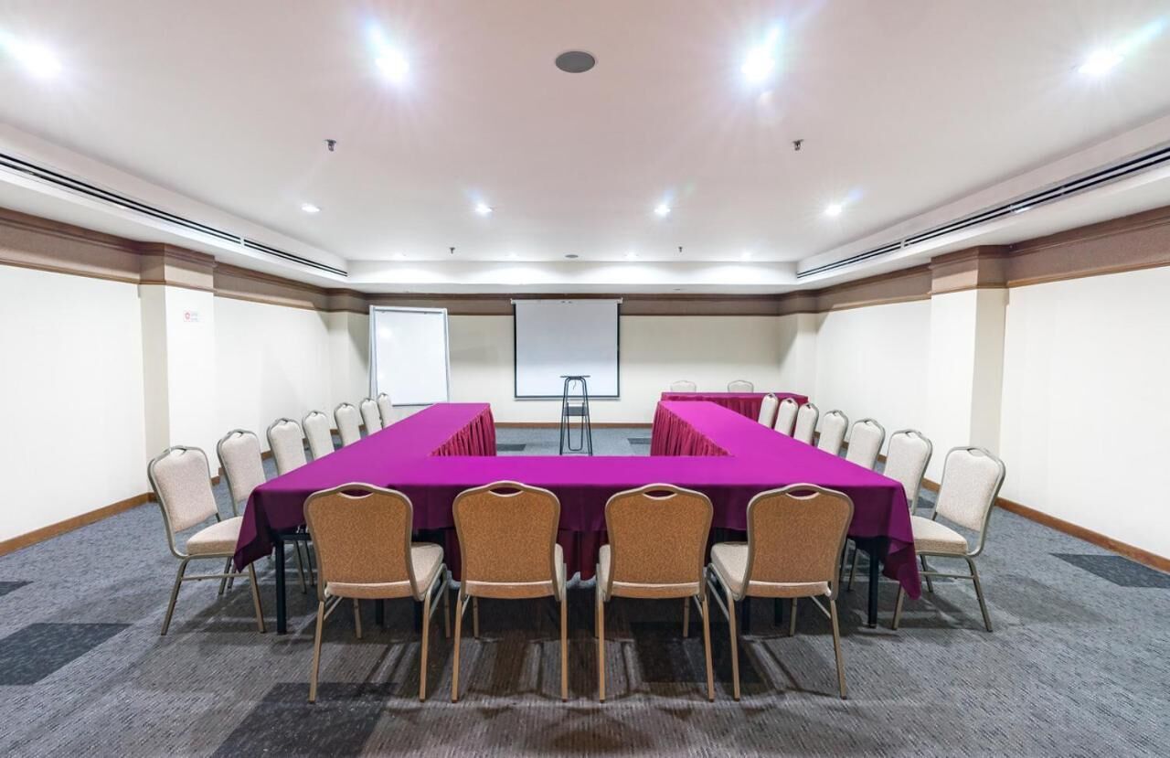 A conference room with a long table, chairs, a projector screen, and a carpeted floor.
