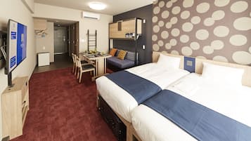 Habitació d'hotel amb literes, escriptori amb cadira, nevera petita i televisió.