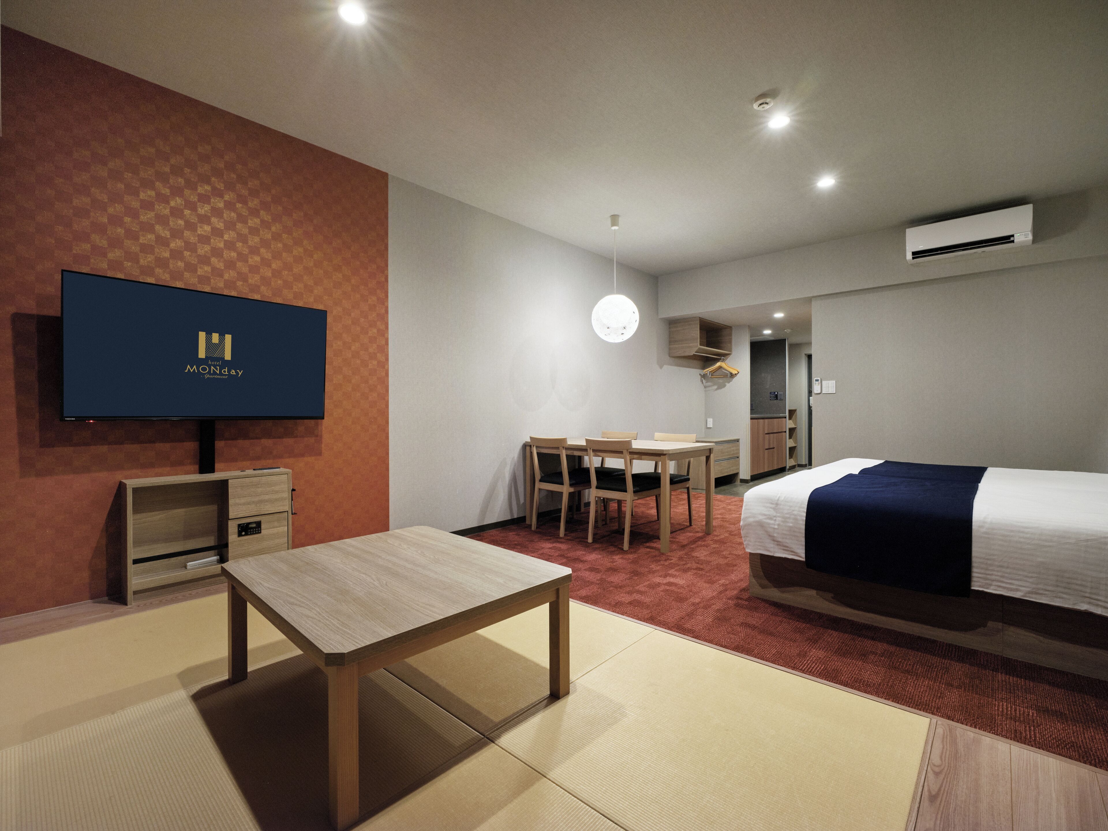 Quarto de hotel com cama, escrivaninha, cadeira, televisão e armário.