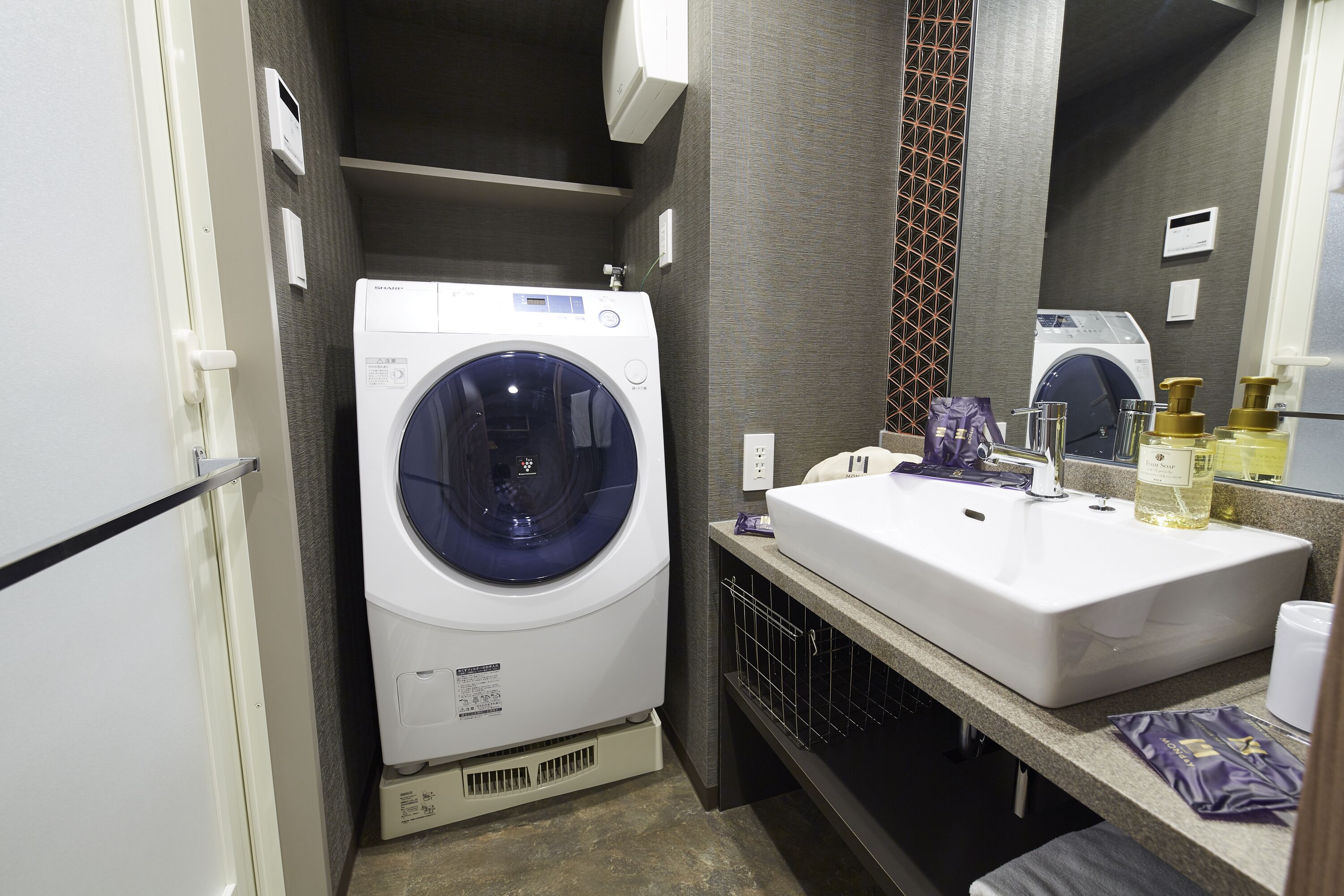 Een compacte hotelbadkamer met een ingebouwde wasmachine, een wastafel en een spiegel.