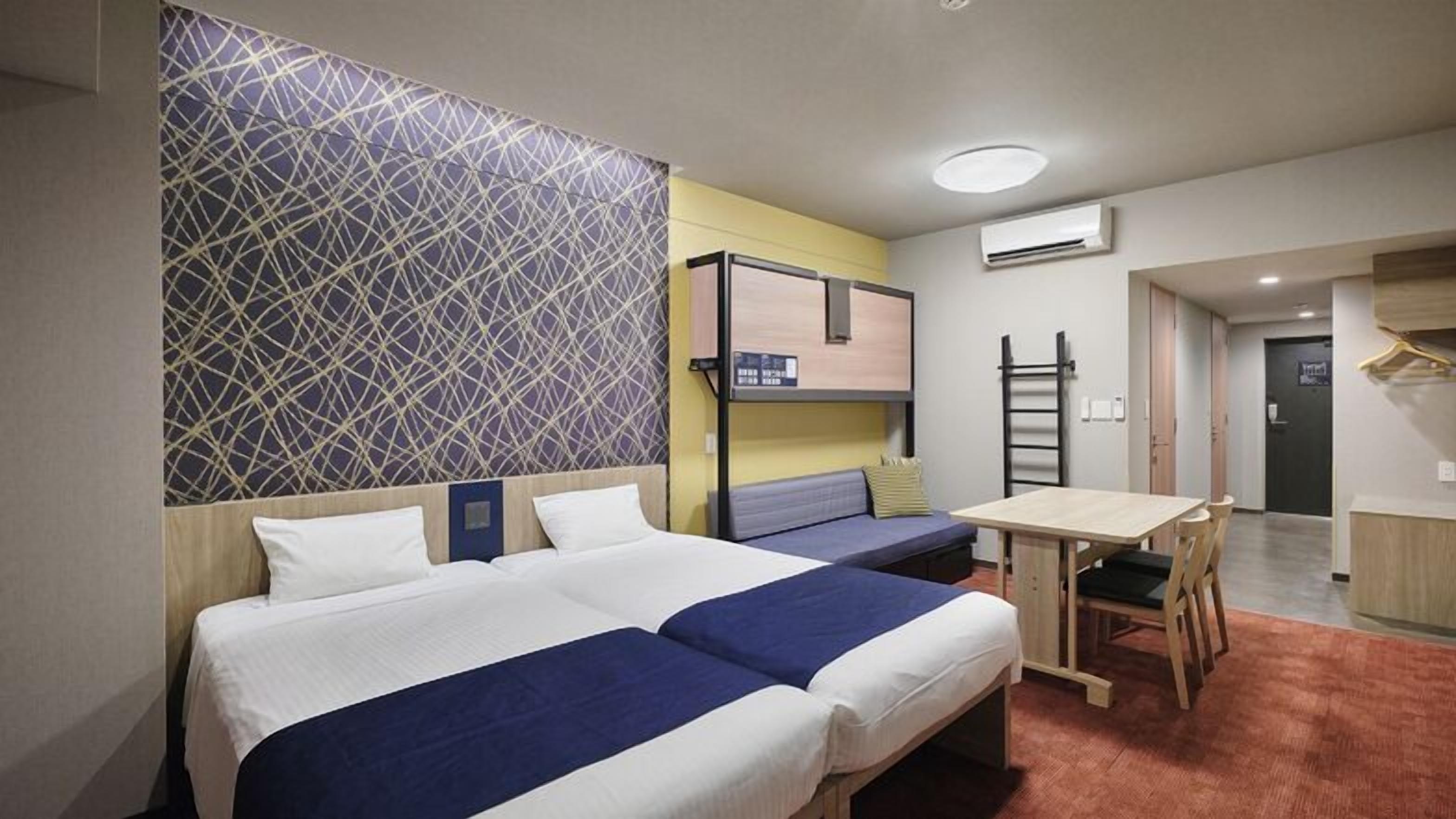 A hotel room with two beds, a desk, and a bunk bed.