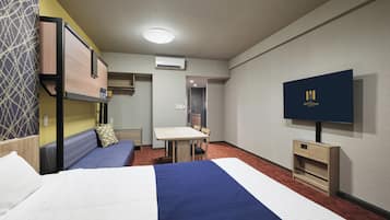 A hotel room with a bunk bed, a desk, a television, and a kitchenette.
