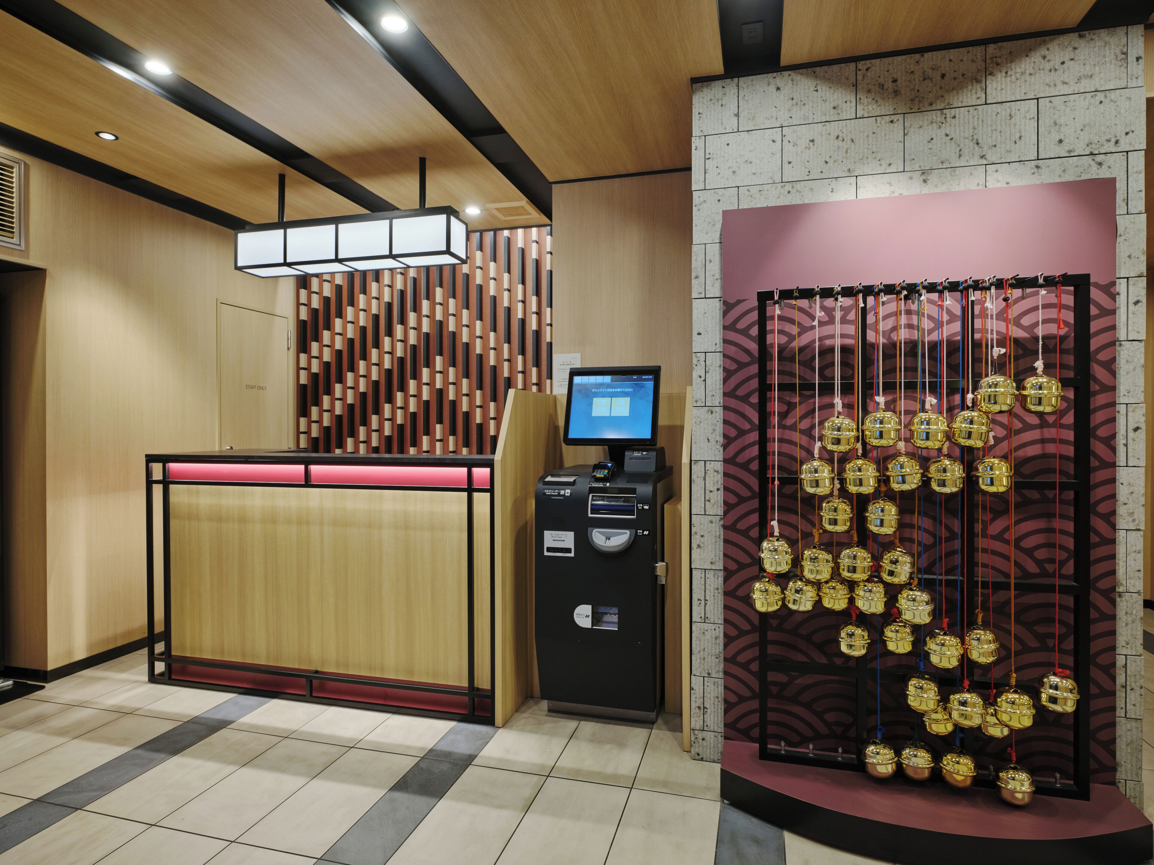 A reception desk with a digital screen, a ticketing machine, and a decorative wall with hanging ornaments.