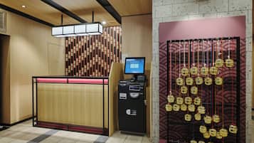 Un comptoir d’accueil doté d’un écran numérique, d’un distributeur de billets et d’un mur décoratif orné d’objets suspendus.